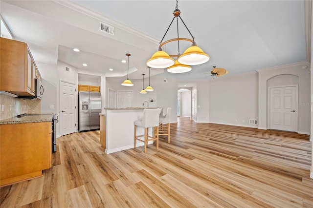 kitchen with light wood-type flooring, a kitchen island, stainless steel appliances, decorative light fixtures, and a kitchen bar