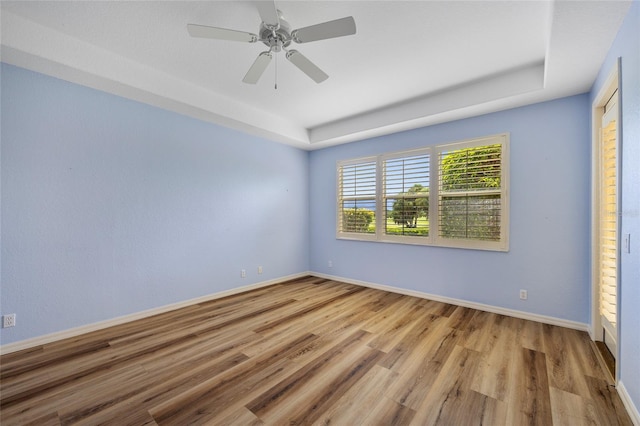 empty room with a raised ceiling, light wood-type flooring, and ceiling fan