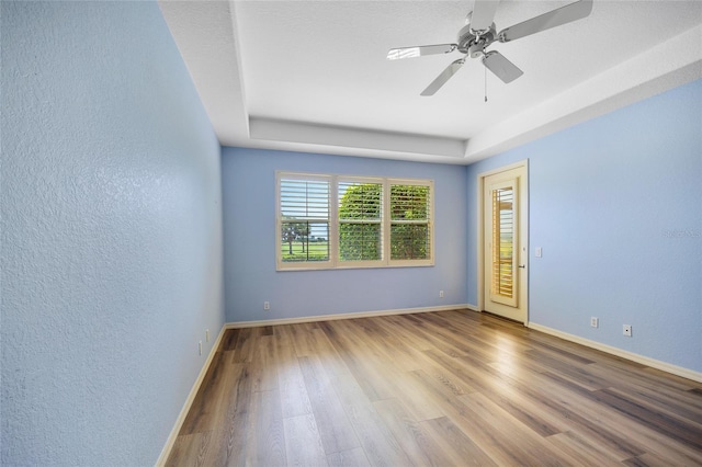 empty room with a tray ceiling, wood-type flooring, and ceiling fan