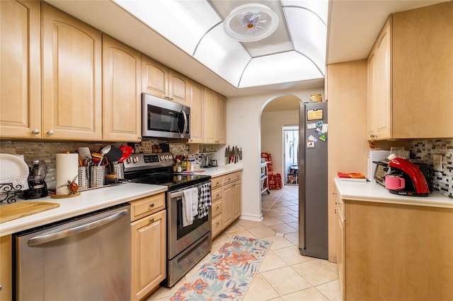 kitchen with light tile patterned floors, appliances with stainless steel finishes, light brown cabinets, and decorative backsplash