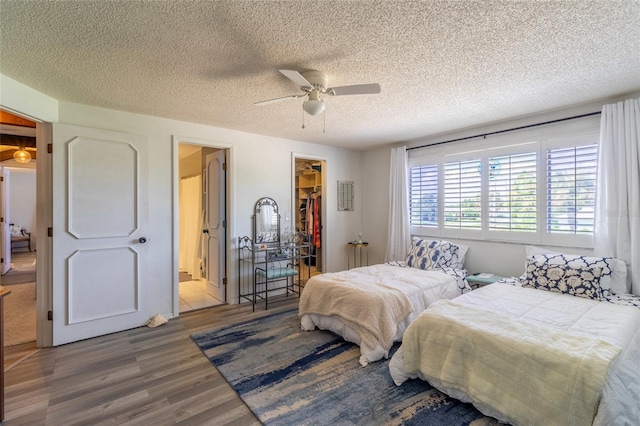 bedroom featuring a walk in closet, a closet, wood-type flooring, ceiling fan, and a textured ceiling