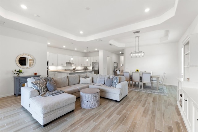 living room with light hardwood / wood-style flooring, a raised ceiling, and a chandelier