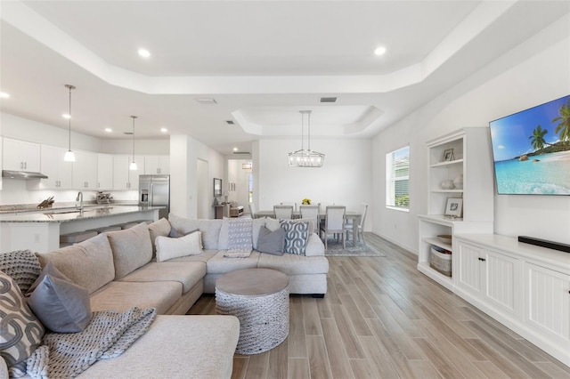 living room with light hardwood / wood-style flooring, an inviting chandelier, and a raised ceiling