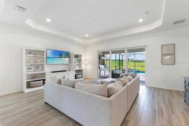 living room featuring light wood-type flooring and a tray ceiling