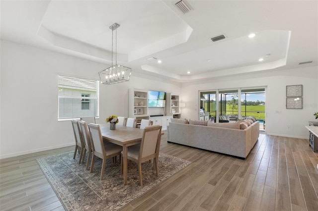 dining room with a raised ceiling, light hardwood / wood-style flooring, and a chandelier