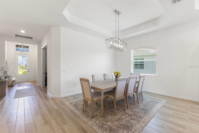 dining room featuring light hardwood / wood-style flooring, a chandelier, and a tray ceiling