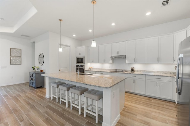 kitchen with white cabinetry, stainless steel appliances, sink, light hardwood / wood-style floors, and a kitchen island with sink