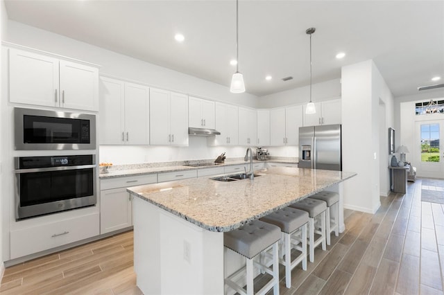 kitchen with appliances with stainless steel finishes, white cabinets, a center island with sink, sink, and light wood-type flooring