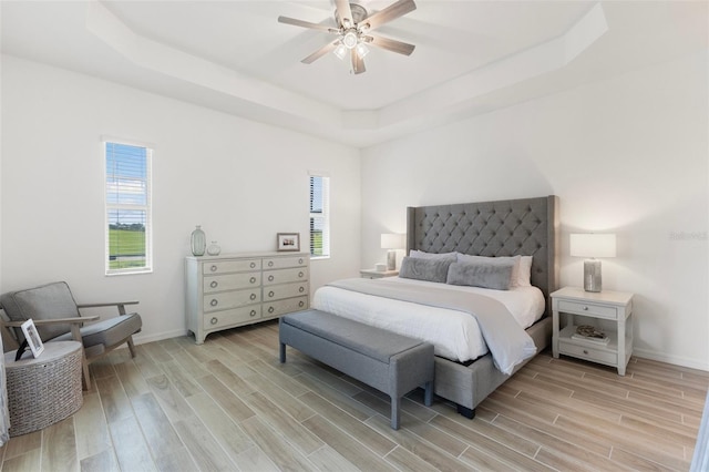 bedroom with multiple windows, ceiling fan, and a raised ceiling