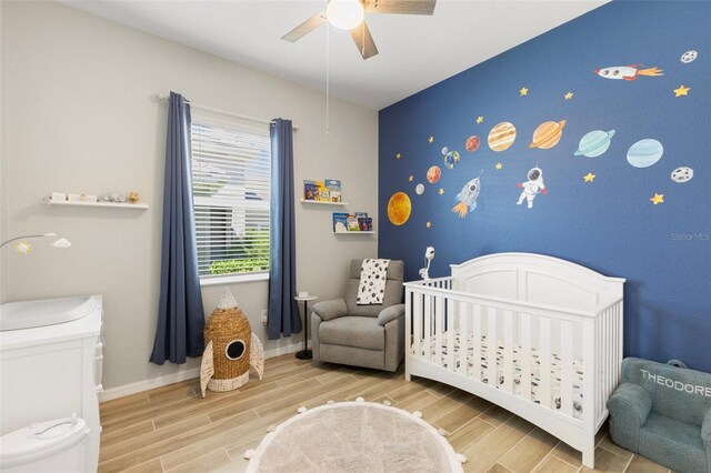 bedroom with light hardwood / wood-style flooring, a nursery area, and ceiling fan