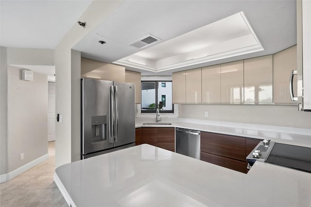 kitchen with light tile patterned floors, cream cabinets, appliances with stainless steel finishes, a raised ceiling, and sink