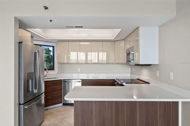 kitchen with light tile patterned flooring, kitchen peninsula, stainless steel appliances, a raised ceiling, and sink