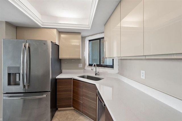 kitchen with appliances with stainless steel finishes, dark brown cabinets, sink, light tile patterned floors, and a tray ceiling