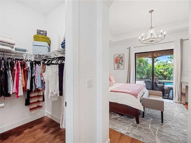 bedroom with a notable chandelier, wood finished floors, baseboards, access to outside, and crown molding