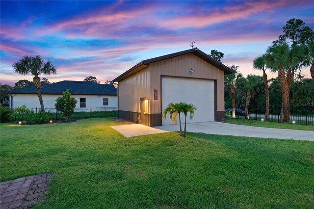 garage at dusk with a garage, fence, and a yard