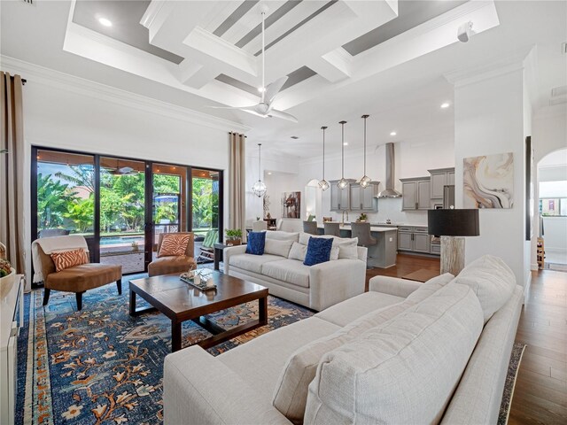 living area with arched walkways, coffered ceiling, a towering ceiling, ornamental molding, and wood finished floors