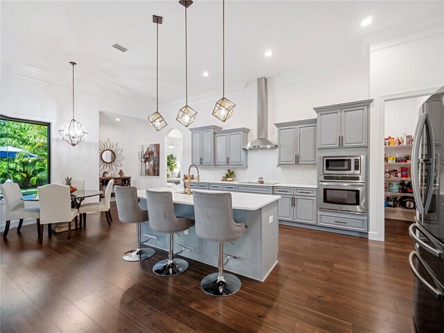 kitchen featuring arched walkways, pendant lighting, light countertops, appliances with stainless steel finishes, and wall chimney exhaust hood