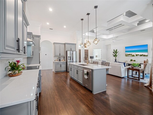 kitchen with appliances with stainless steel finishes, open floor plan, decorative light fixtures, a kitchen island with sink, and light countertops