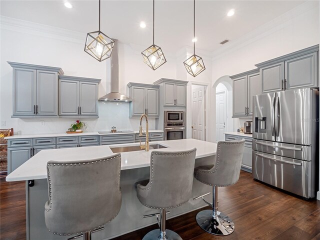 kitchen featuring a kitchen island with sink, light countertops, appliances with stainless steel finishes, wall chimney exhaust hood, and pendant lighting