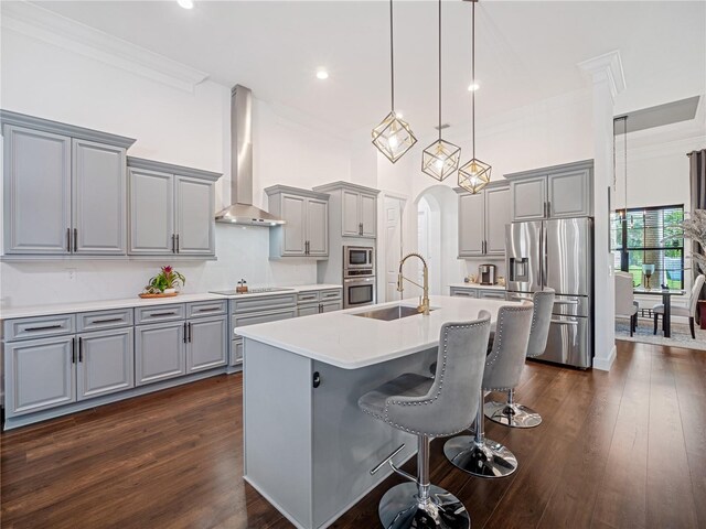 kitchen with a sink, light countertops, appliances with stainless steel finishes, wall chimney exhaust hood, and an island with sink