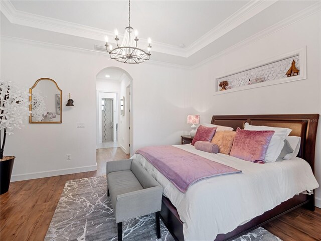 bedroom featuring arched walkways, a tray ceiling, dark wood-type flooring, ornamental molding, and baseboards