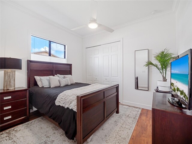 bedroom featuring wood finished floors, a ceiling fan, baseboards, a closet, and crown molding