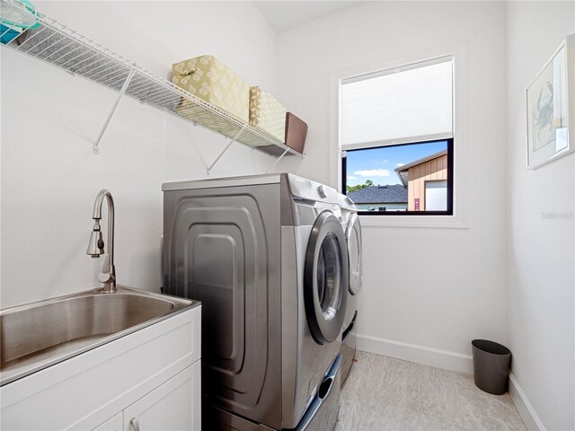 clothes washing area with a sink, washing machine and clothes dryer, cabinet space, and baseboards