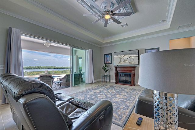 tiled living room with ceiling fan, ornamental molding, and a raised ceiling