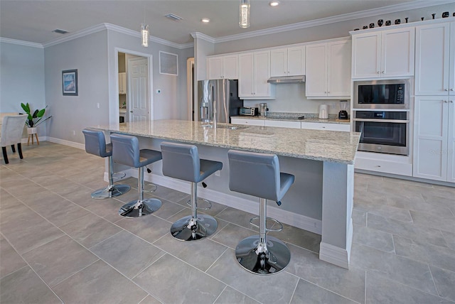 kitchen with a breakfast bar, white cabinetry, ornamental molding, a kitchen island with sink, and stainless steel appliances