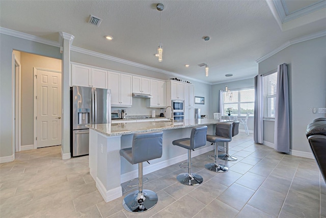 kitchen with appliances with stainless steel finishes, white cabinetry, a kitchen bar, hanging light fixtures, and a kitchen island with sink