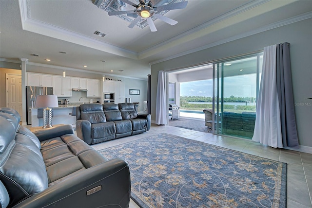 living room featuring light tile patterned flooring, sink, ornamental molding, ceiling fan, and a raised ceiling