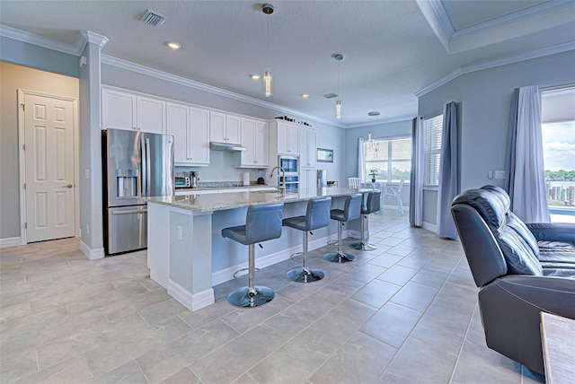 kitchen featuring pendant lighting, white cabinetry, a kitchen island with sink, stainless steel fridge with ice dispenser, and light stone countertops