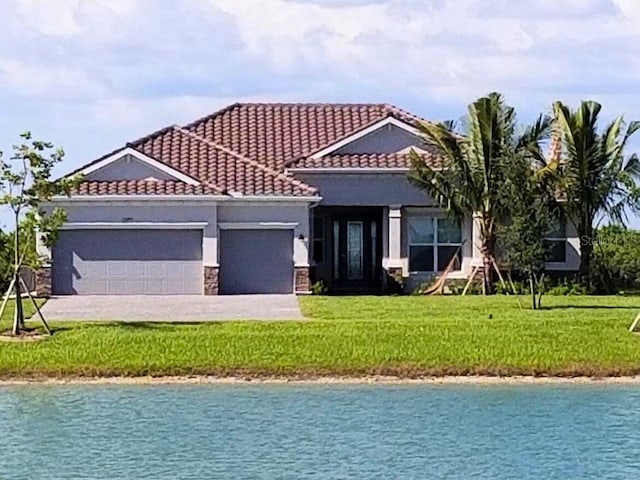 15240 Spanish Point Dr, Port Charlotte, FL 33981 - view of front of property with a water view, a garage, a tile roof, stucco siding, and a front lawn