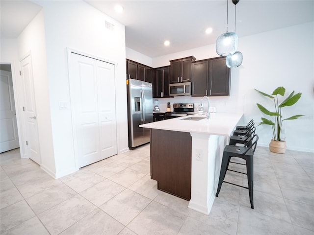 kitchen with appliances with stainless steel finishes, pendant lighting, kitchen peninsula, dark brown cabinetry, and light tile patterned flooring