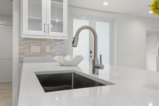 room details with light stone counters, white cabinets, sink, and backsplash