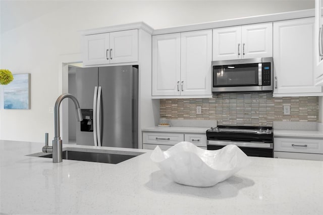 kitchen with white cabinetry, appliances with stainless steel finishes, light stone counters, and backsplash