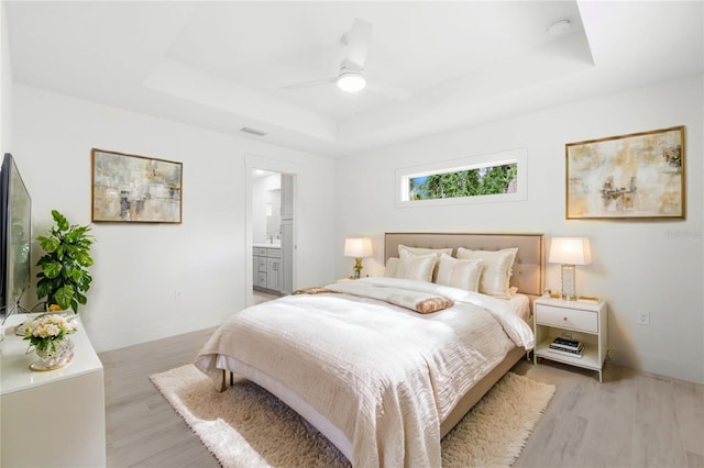 bedroom featuring a raised ceiling, ensuite bathroom, ceiling fan, and light hardwood / wood-style floors