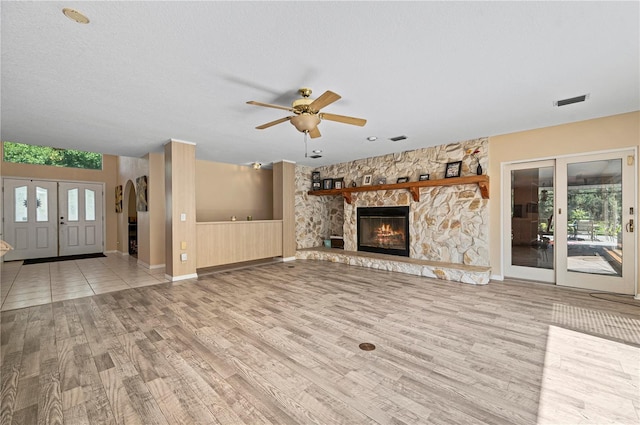 unfurnished living room with french doors, a textured ceiling, ceiling fan, light hardwood / wood-style floors, and a fireplace