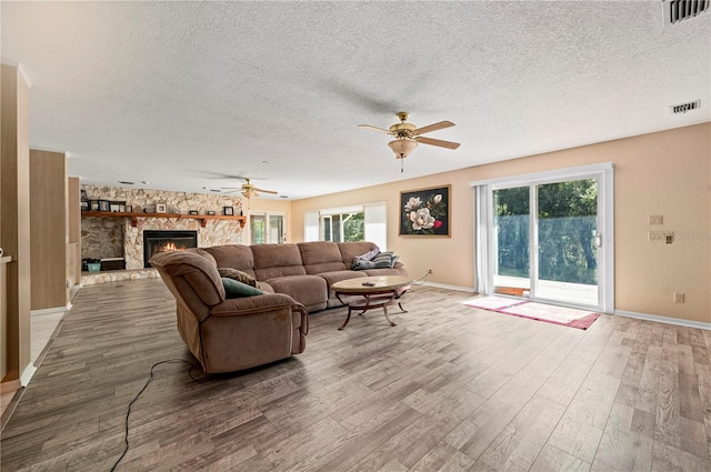 living room with a textured ceiling, a stone fireplace, and hardwood / wood-style floors