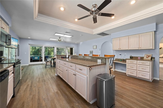 kitchen featuring hardwood / wood-style flooring, a tray ceiling, an island with sink, and ceiling fan