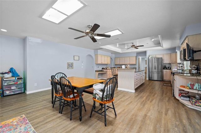 dining room with sink, ceiling fan, light hardwood / wood-style flooring, and a tray ceiling