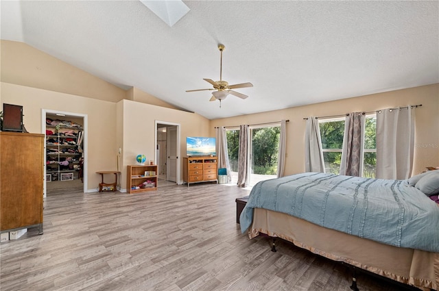 bedroom with ceiling fan, vaulted ceiling with skylight, light wood-type flooring, and a walk in closet