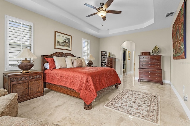 tiled bedroom featuring ceiling fan and a tray ceiling