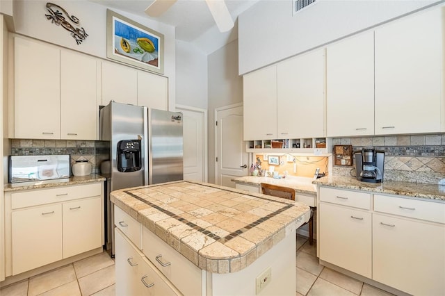 kitchen featuring a center island, tasteful backsplash, white cabinets, light tile patterned flooring, and stainless steel fridge