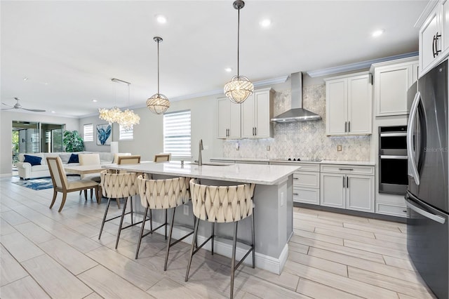 kitchen with stainless steel appliances, a healthy amount of sunlight, an island with sink, and wall chimney range hood