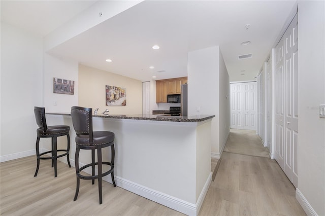 kitchen featuring a breakfast bar, dark stone counters, black appliances, light hardwood / wood-style flooring, and kitchen peninsula