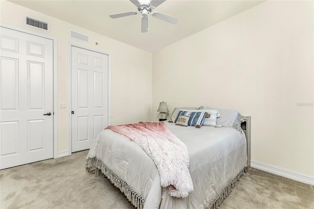 bedroom featuring ceiling fan, light colored carpet, and two closets