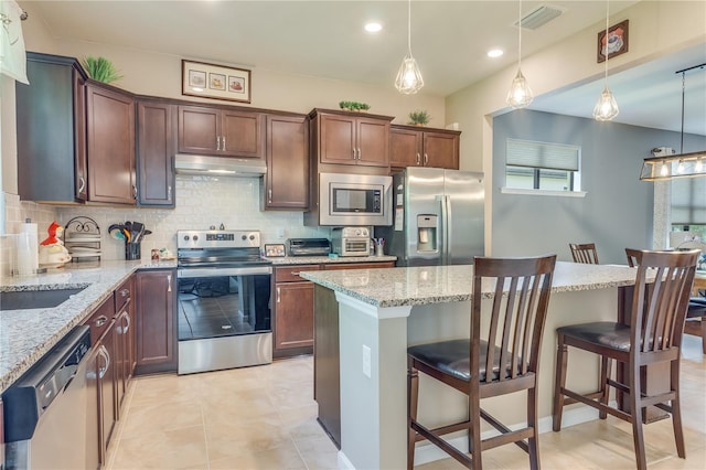 kitchen with light tile patterned flooring, light stone counters, pendant lighting, and stainless steel appliances