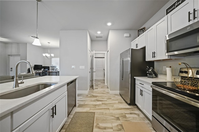 kitchen with sink, appliances with stainless steel finishes, hanging light fixtures, and white cabinets