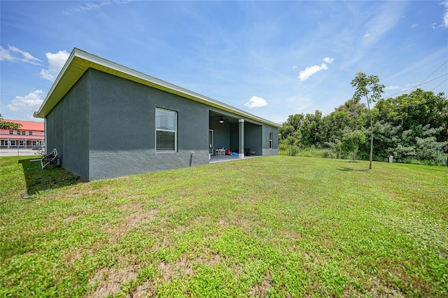 back of property with a patio area, ceiling fan, a lawn, and stucco siding